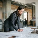Chef de projet immobilier femme examinant des plans architecturaux dans un bureau moderne avec maquettes de bâtiments